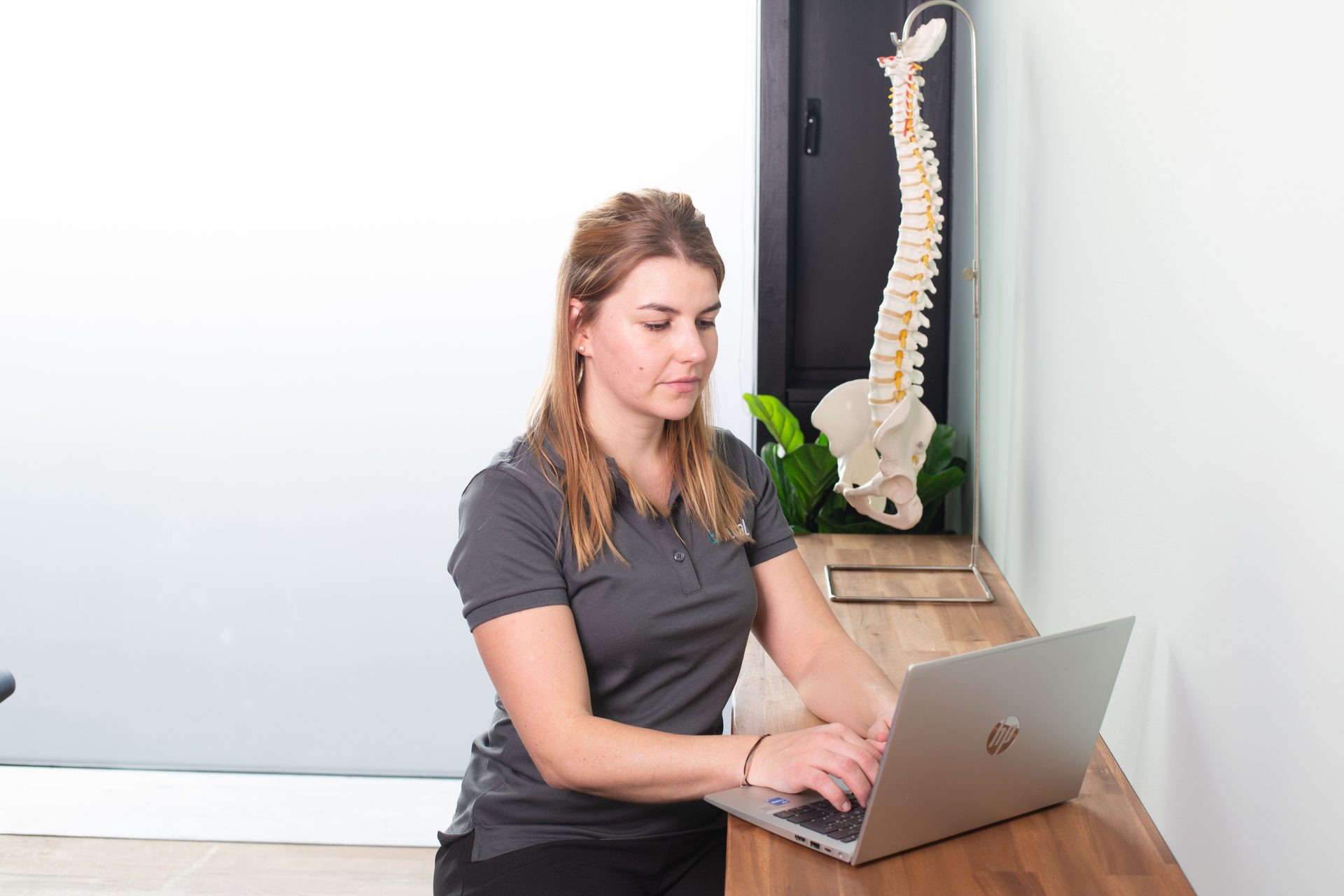 Woman typing on laptop next to a spine model.