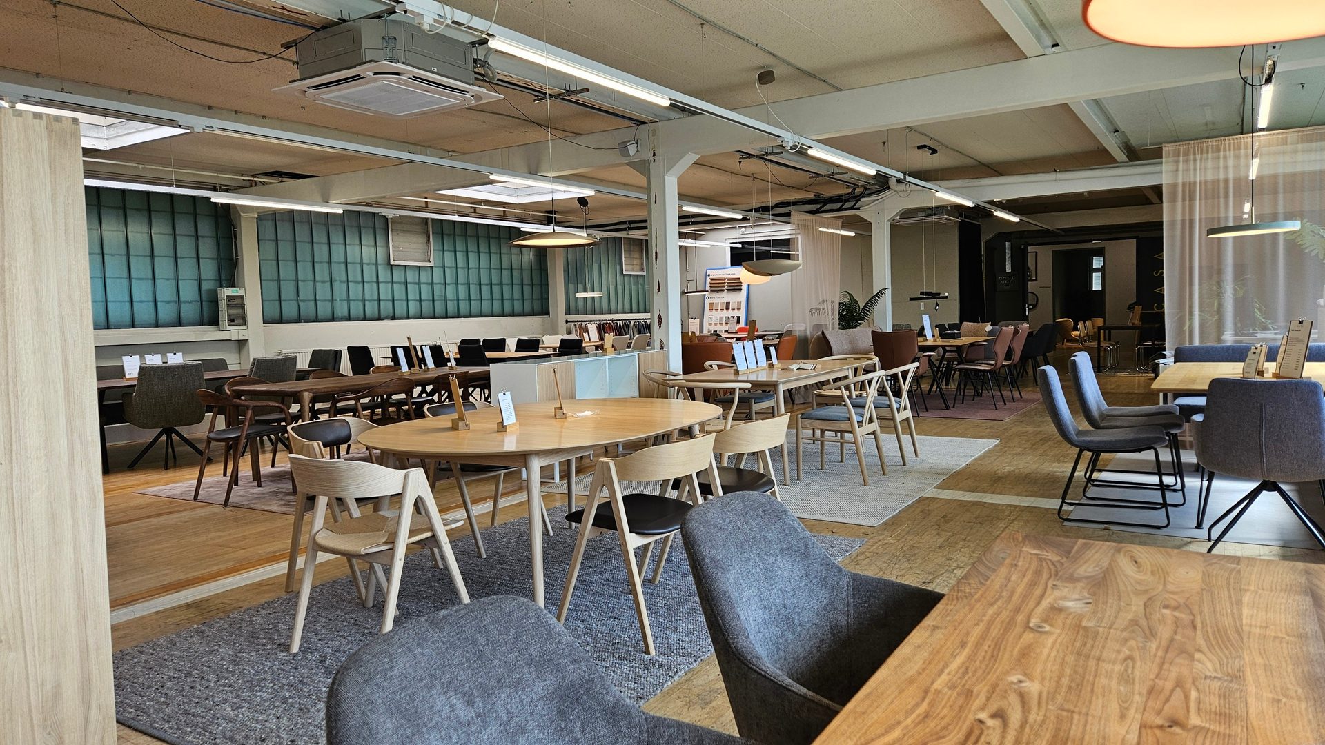 A spacious, brightly lit modern furniture showroom with various wooden tables and chairs, and open-plan layout.