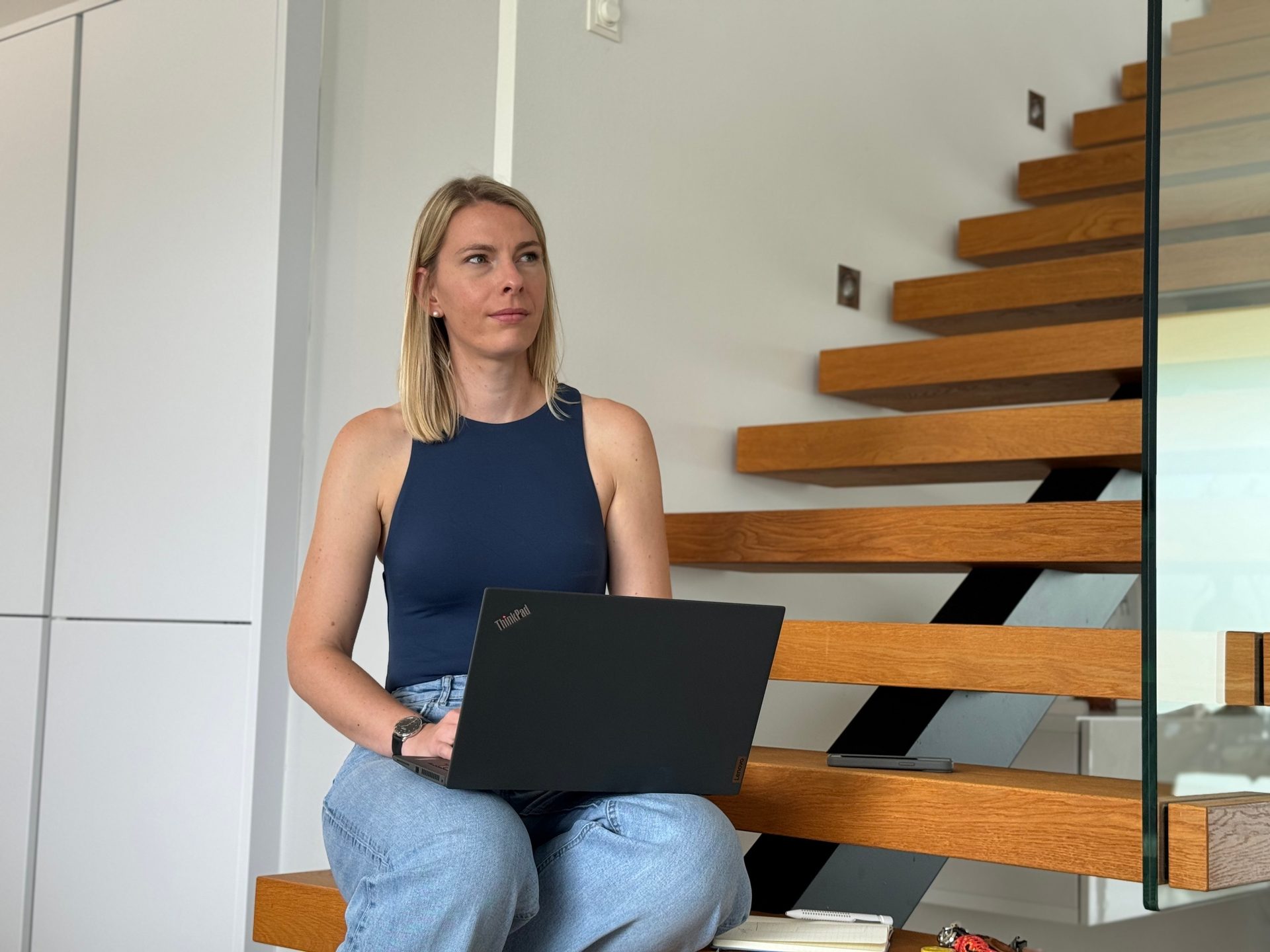 Woman sitting on modern wooden stairs, holding a laptop.