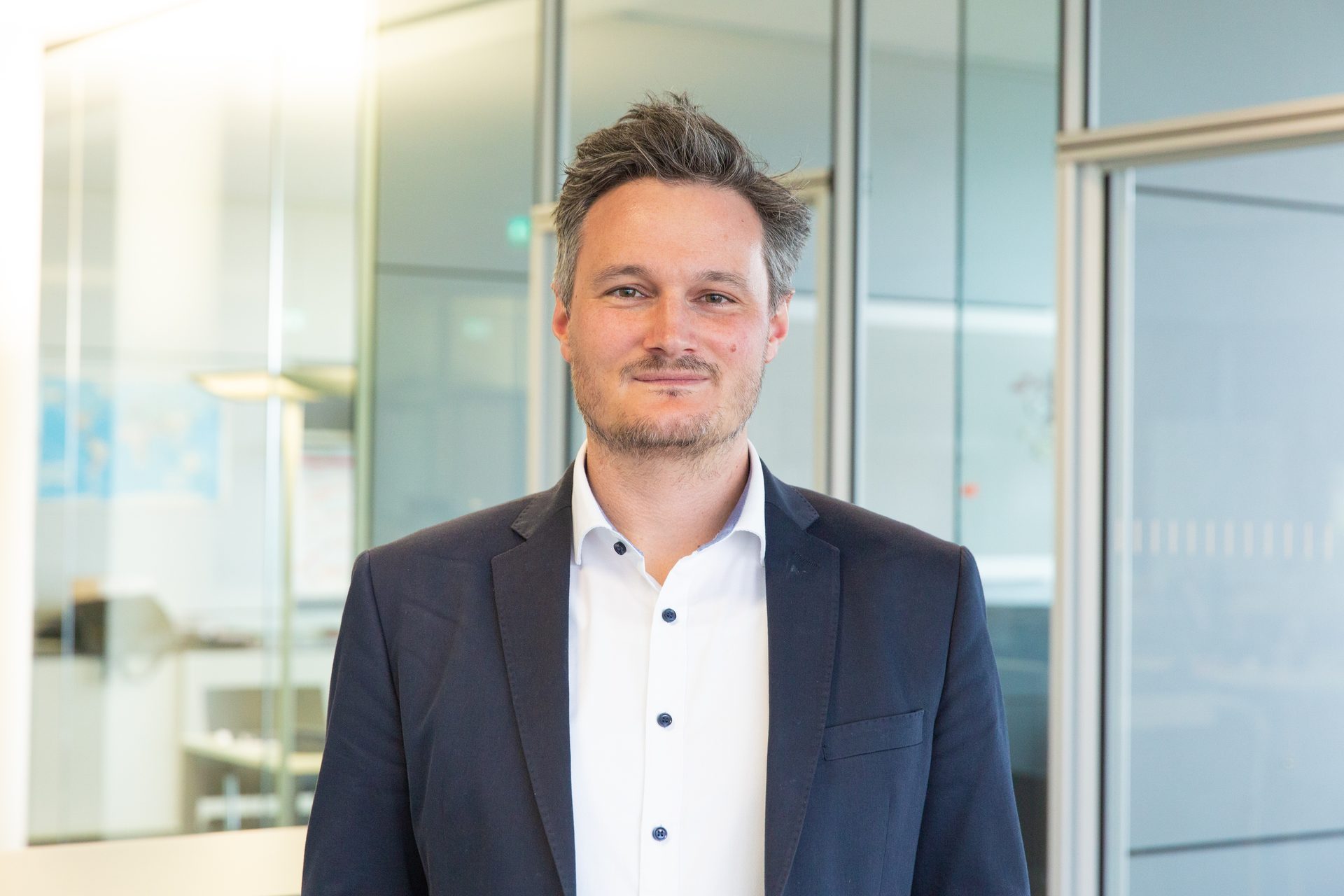Smiling man in a suit, professional headshot in an office.