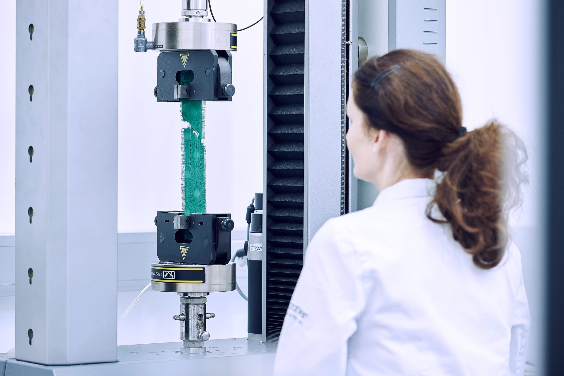 Scientist observing a green textile undergoing tensile testing.