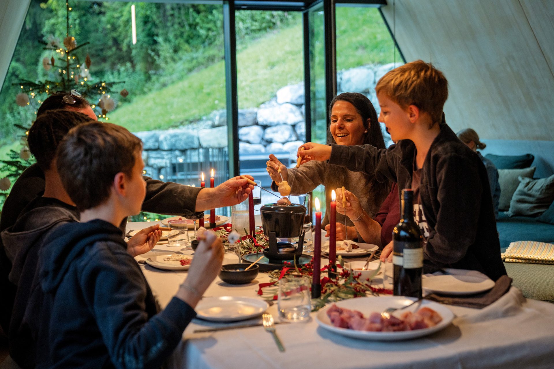 Family enjoying fondue around a festive table with candles and a Christmas tree.
