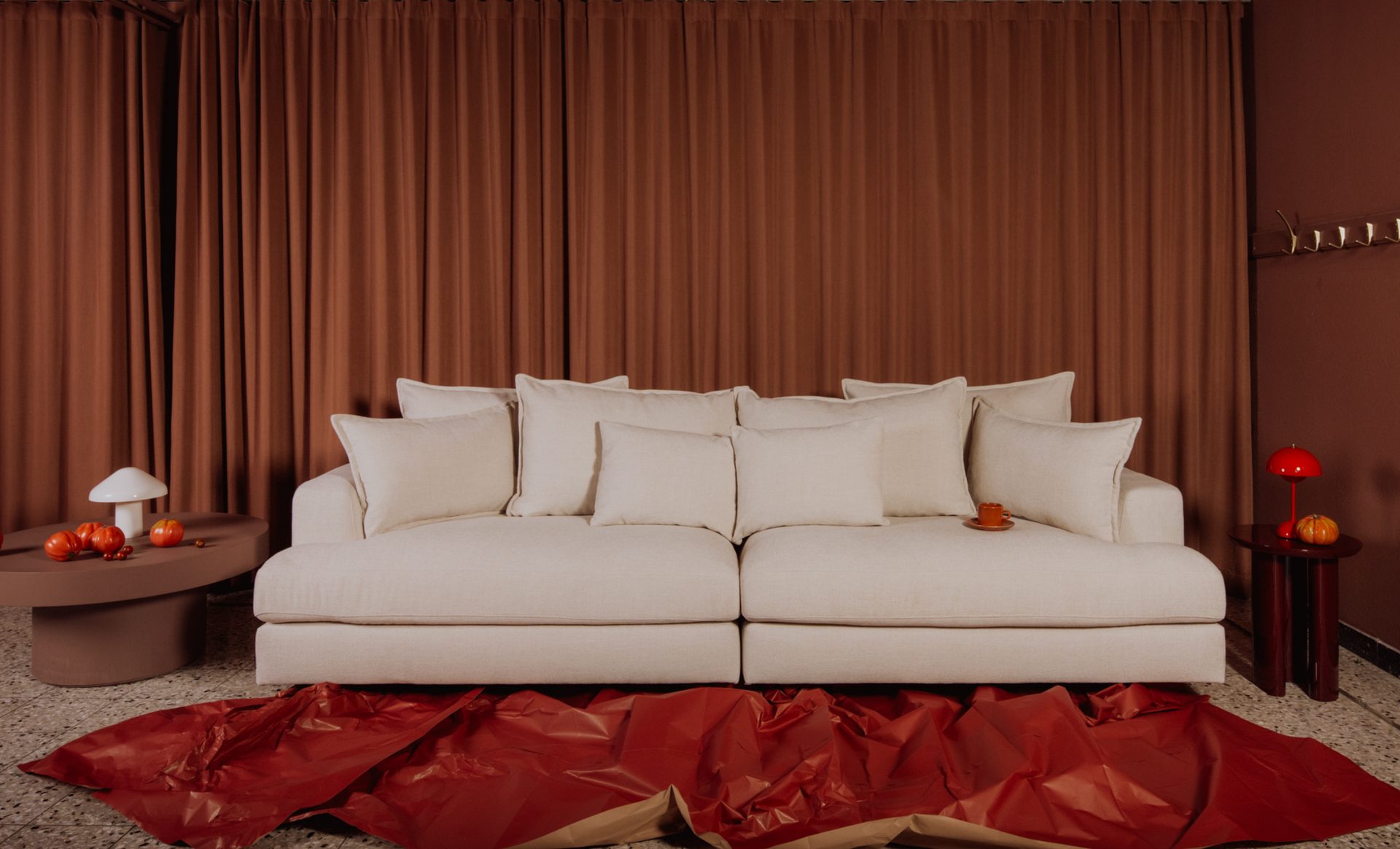 A modern living room featuring a large white sofa, rich brown curtains, and minimalist red accents.