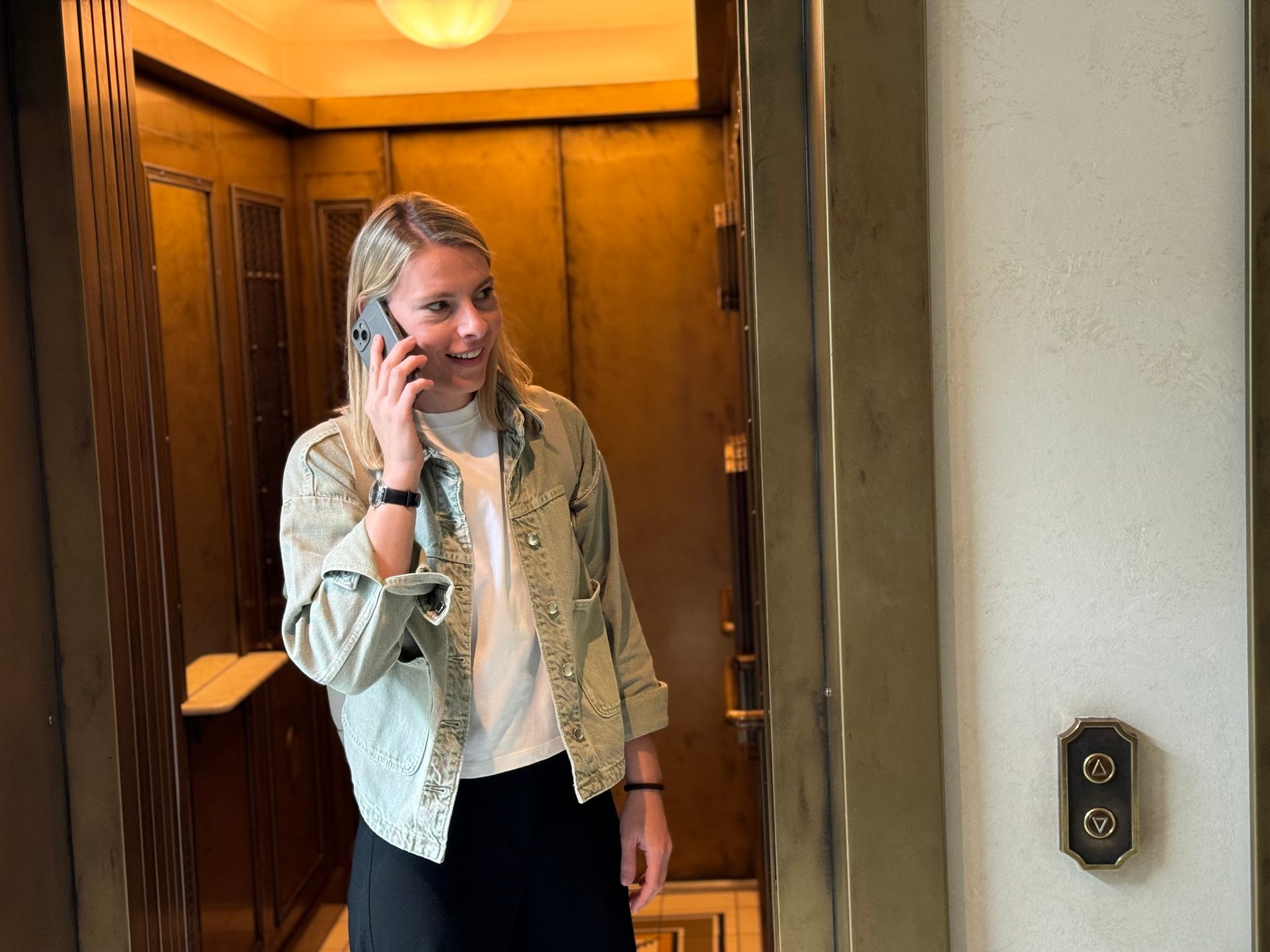 Blonde woman on phone in ornate gold elevator.