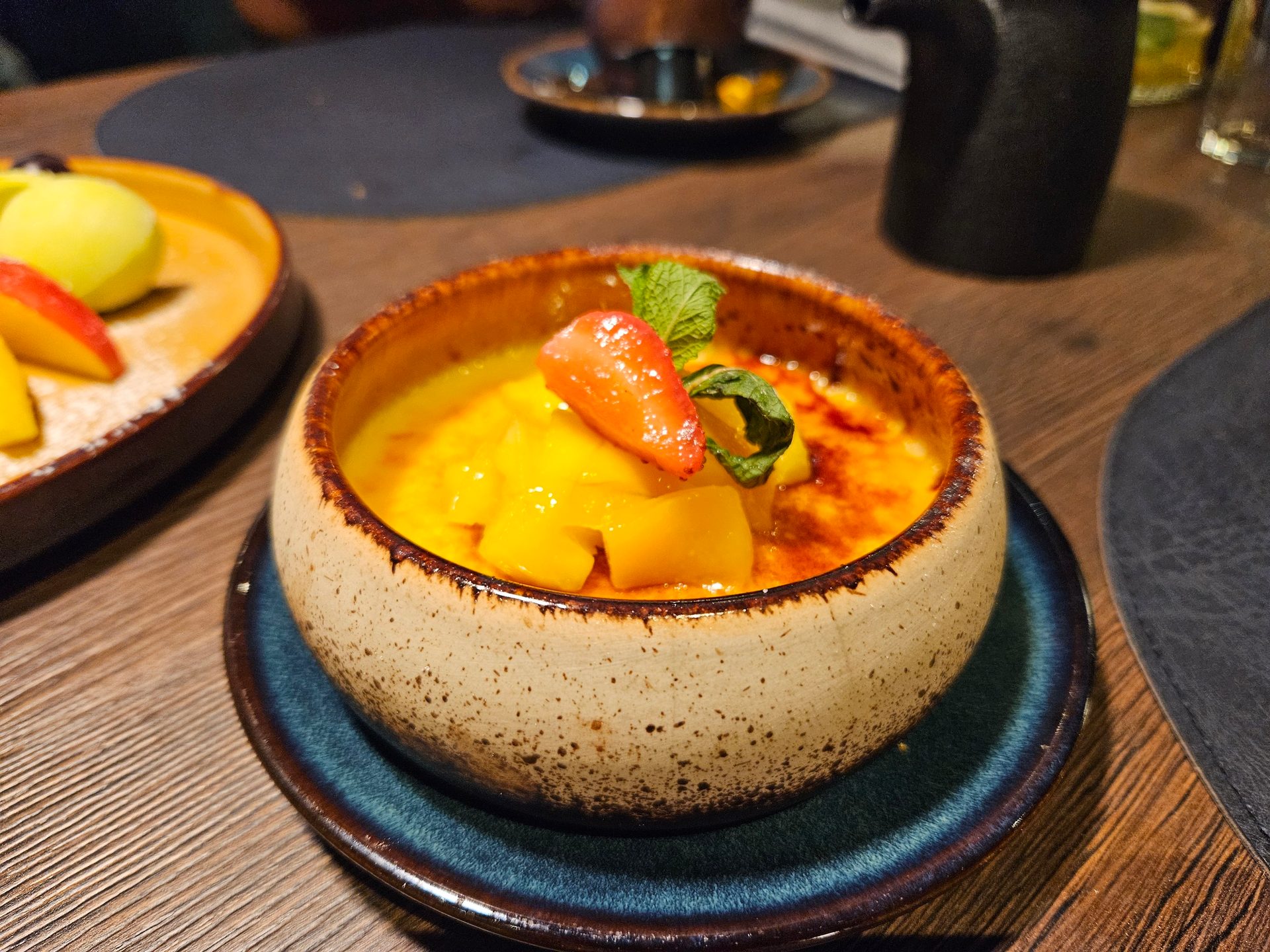 Dessert: Mango creme brulee with mango chunks, strawberry, and mint in a rustic bowl.
