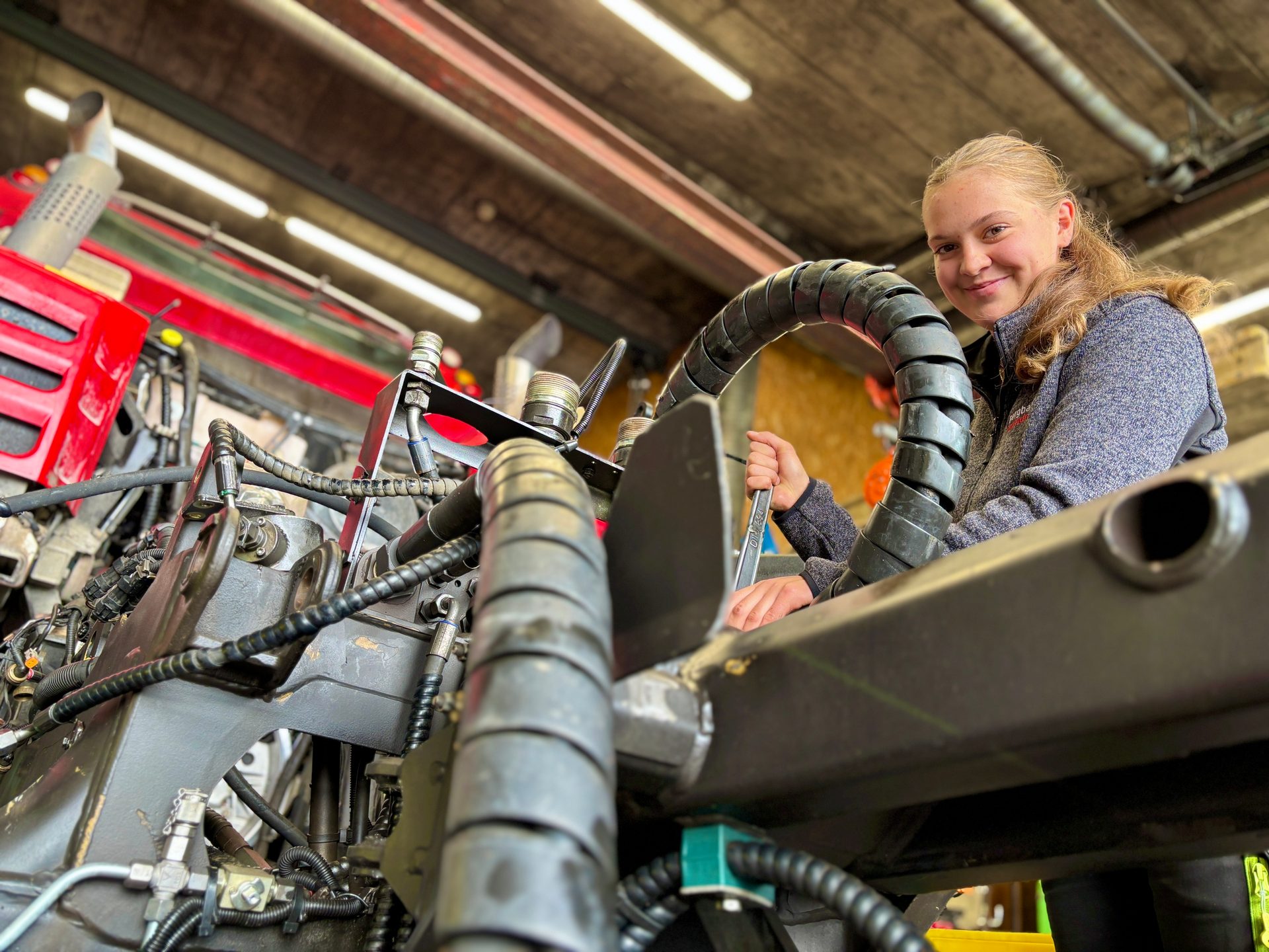 Young woman working on complex machinery, smiling at the camera.