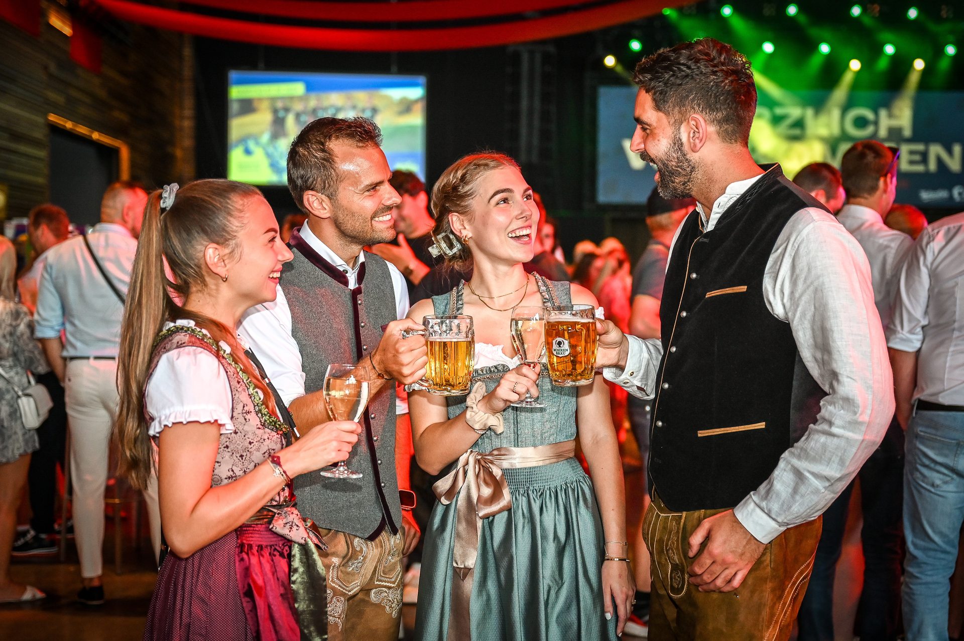 Four people in Dirndl and Lederhosen toast with drinks.
