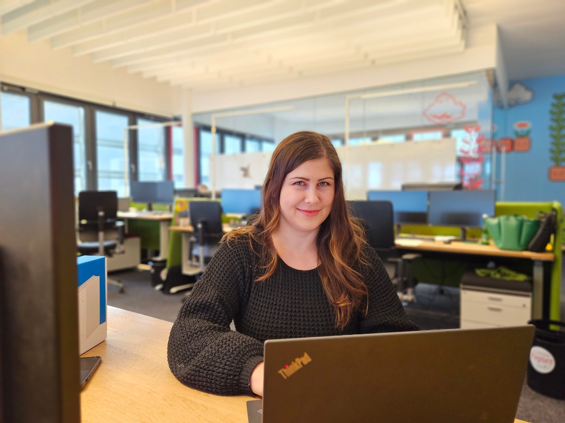 Smiling woman works on laptop at office desk.