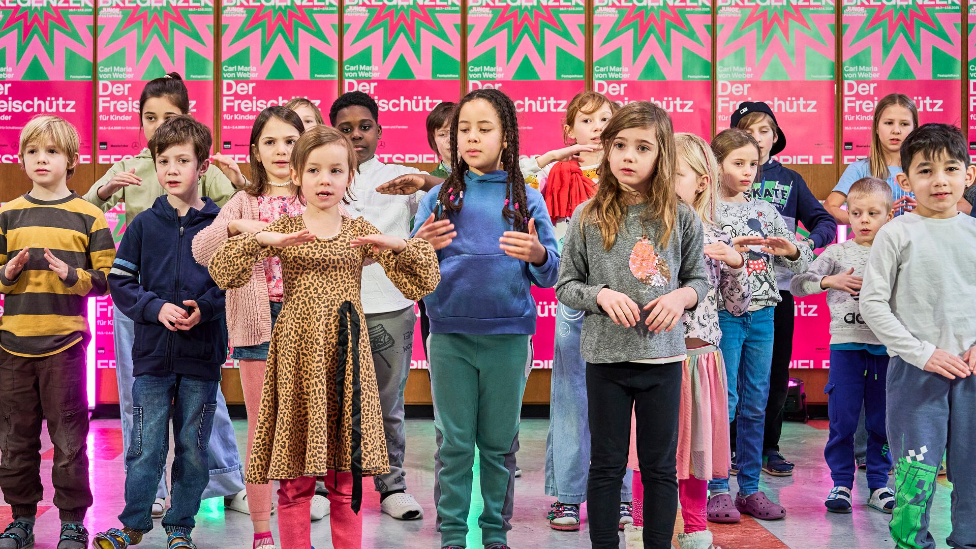 Children performing with synchronized hand gestures, likely rehearsing for the "Der Freischütz für Kinder" opera.