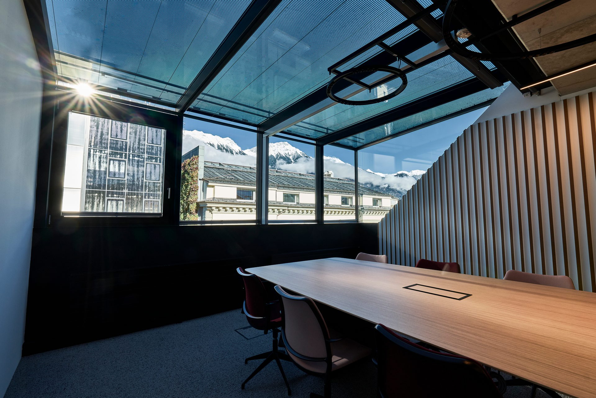 Modern meeting room with panoramic views of snow-capped mountains through a glass roof and large windows.