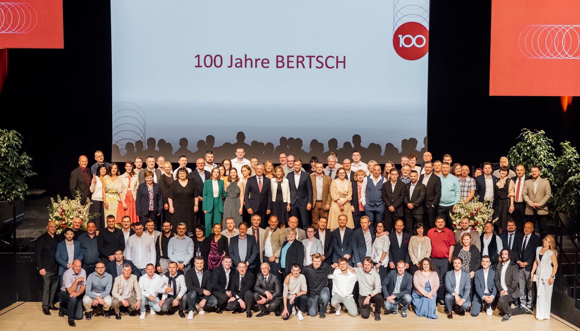 Group photo of BERTSCH employees on stage, with "100 Jahre BERTSCH" on screen.
