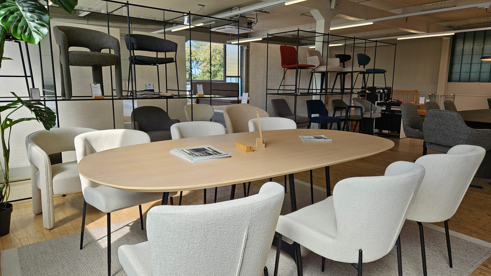Modern furniture showroom with an oval table, white chairs, and display shelves featuring various seating.