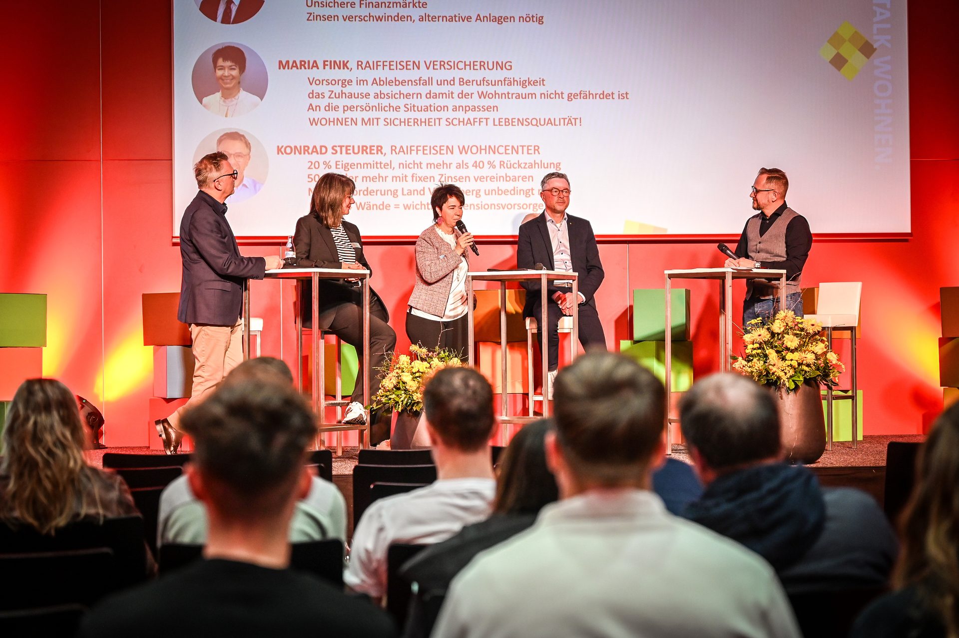 Panel discussion with five speakers on stage and presentation slides, 'TALK WOHNEN' event.