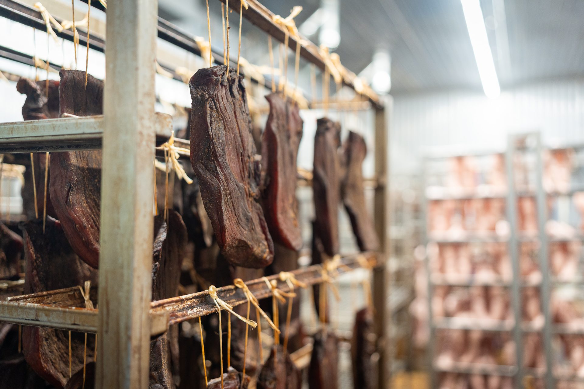 Cured meats hanging on metal racks in a production facility.