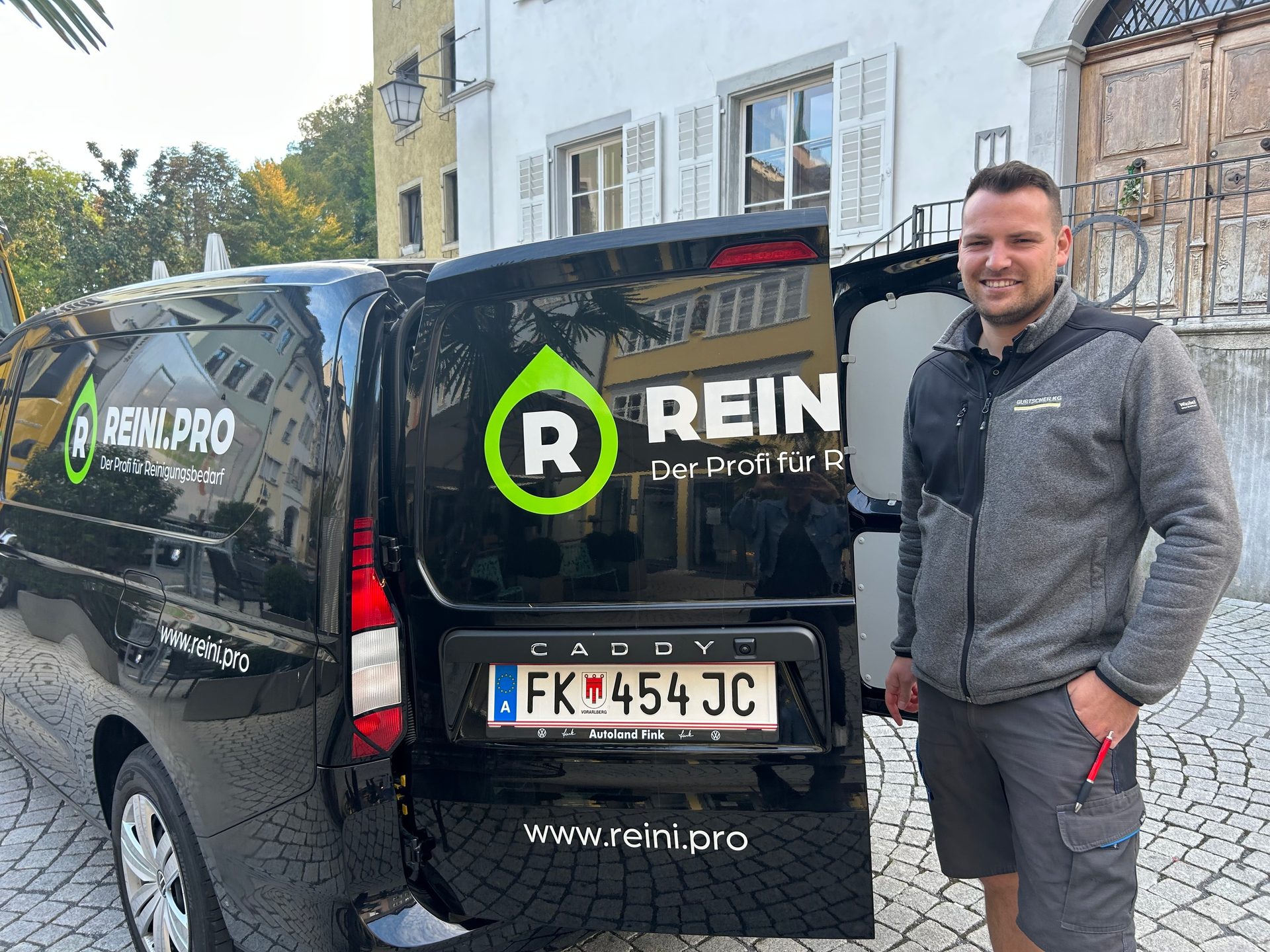 A man stands proudly beside a black Reini.pro delivery van, showcasing the cleaning supply brand.