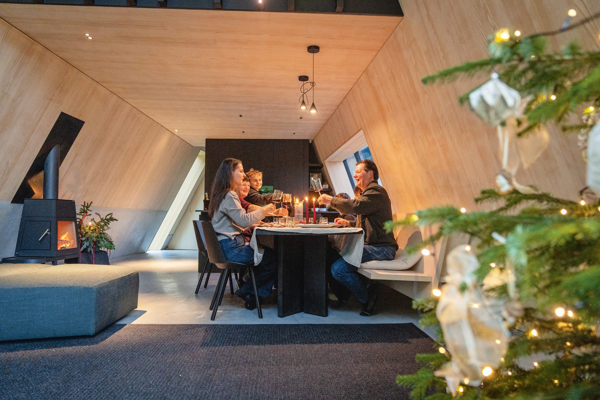 Family celebrates Christmas dinner in a modern home with a fireplace and festive tree.