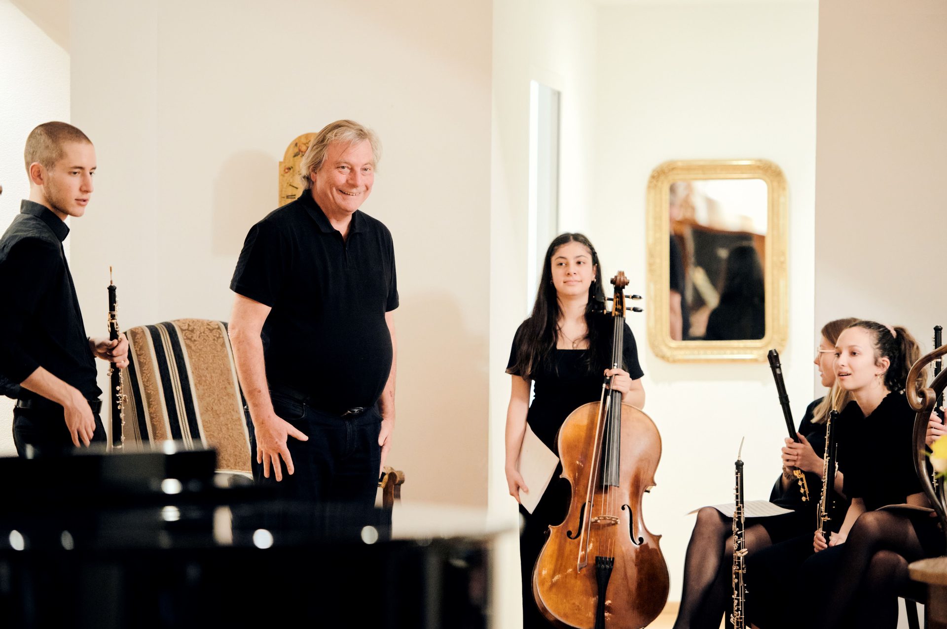 A group of musicians, including a cellist and oboe players, with a smiling man.