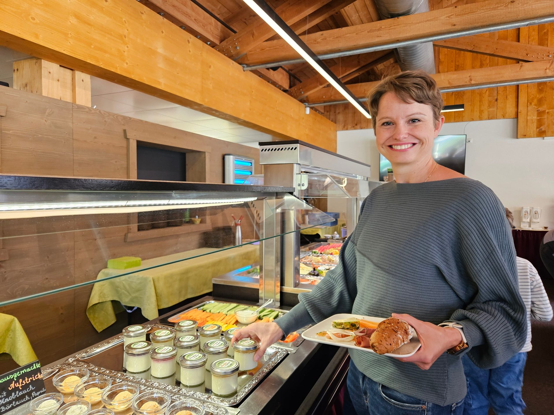 Smiling woman holding a plate of food, reaching for an item at a buffet.