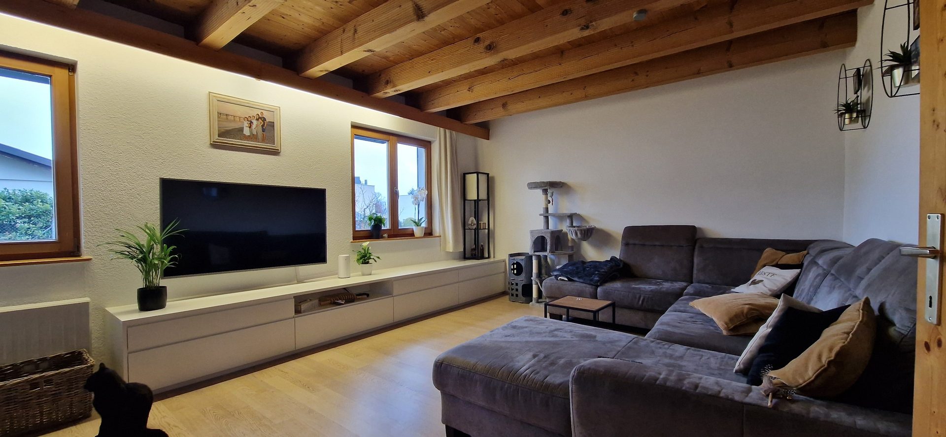 A modern living room with a large grey sectional sofa, TV on a console, and a rustic wooden beamed ceiling.