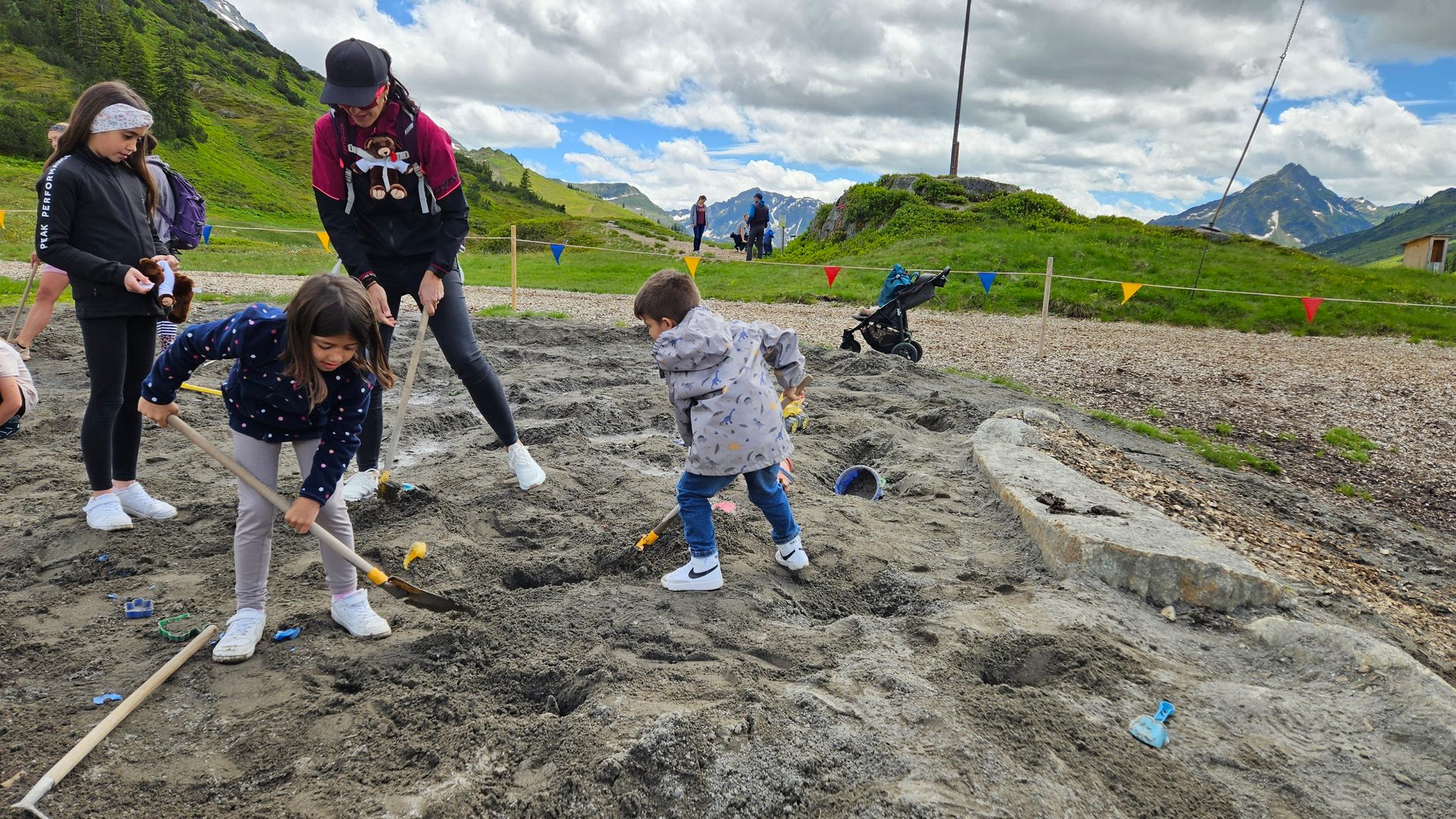 Group of people digging in sand with shovels in a mountainous landscape.