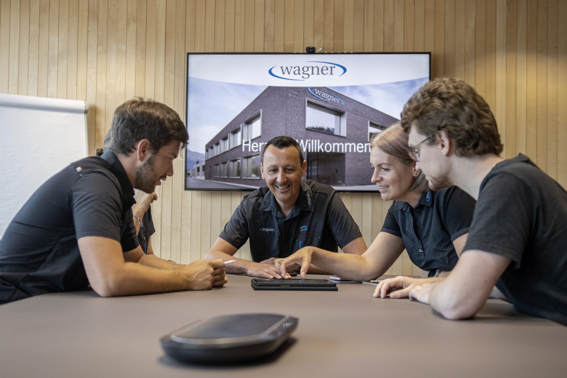 Four colleagues are discussing information on a tablet during a business meeting at Wagner.