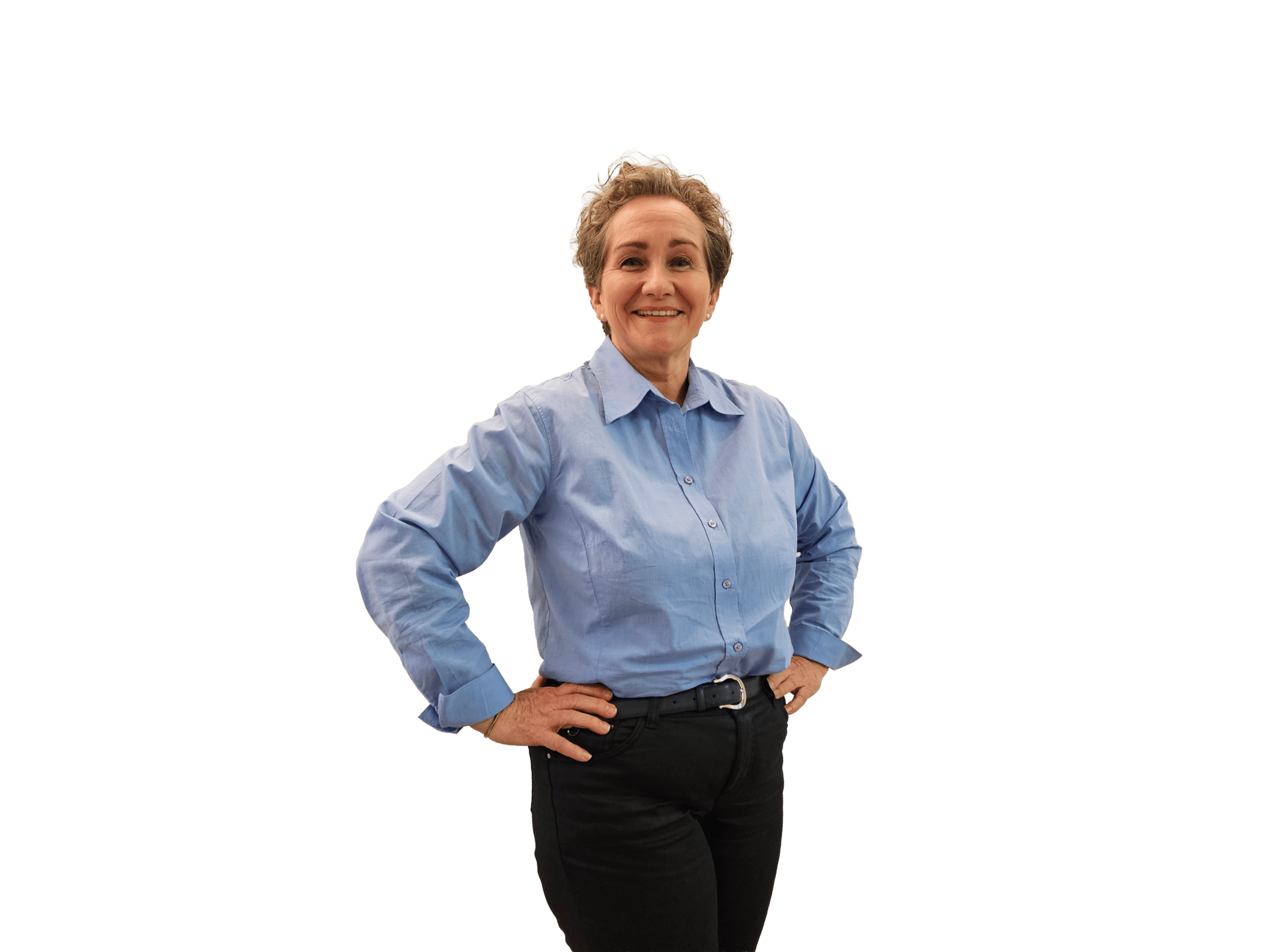Smiling older woman in a blue shirt and black pants, standing with hands on her hips.