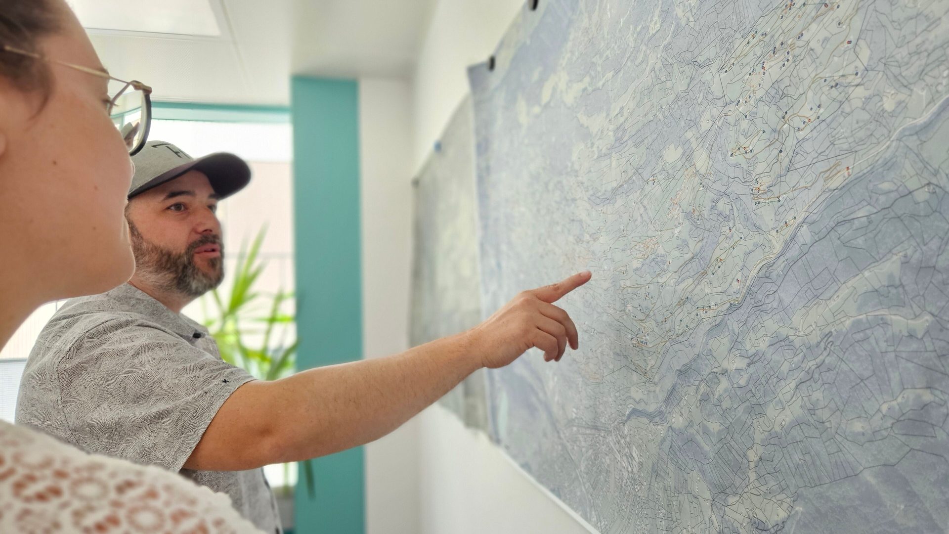 A man and a woman look at a large map on a wall, the man pointing to a specific location.