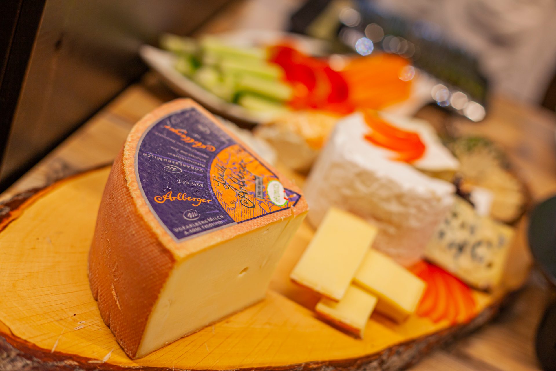 A selection of cheeses on a wooden board, with a large Arlberger cheese wedge in the foreground.
