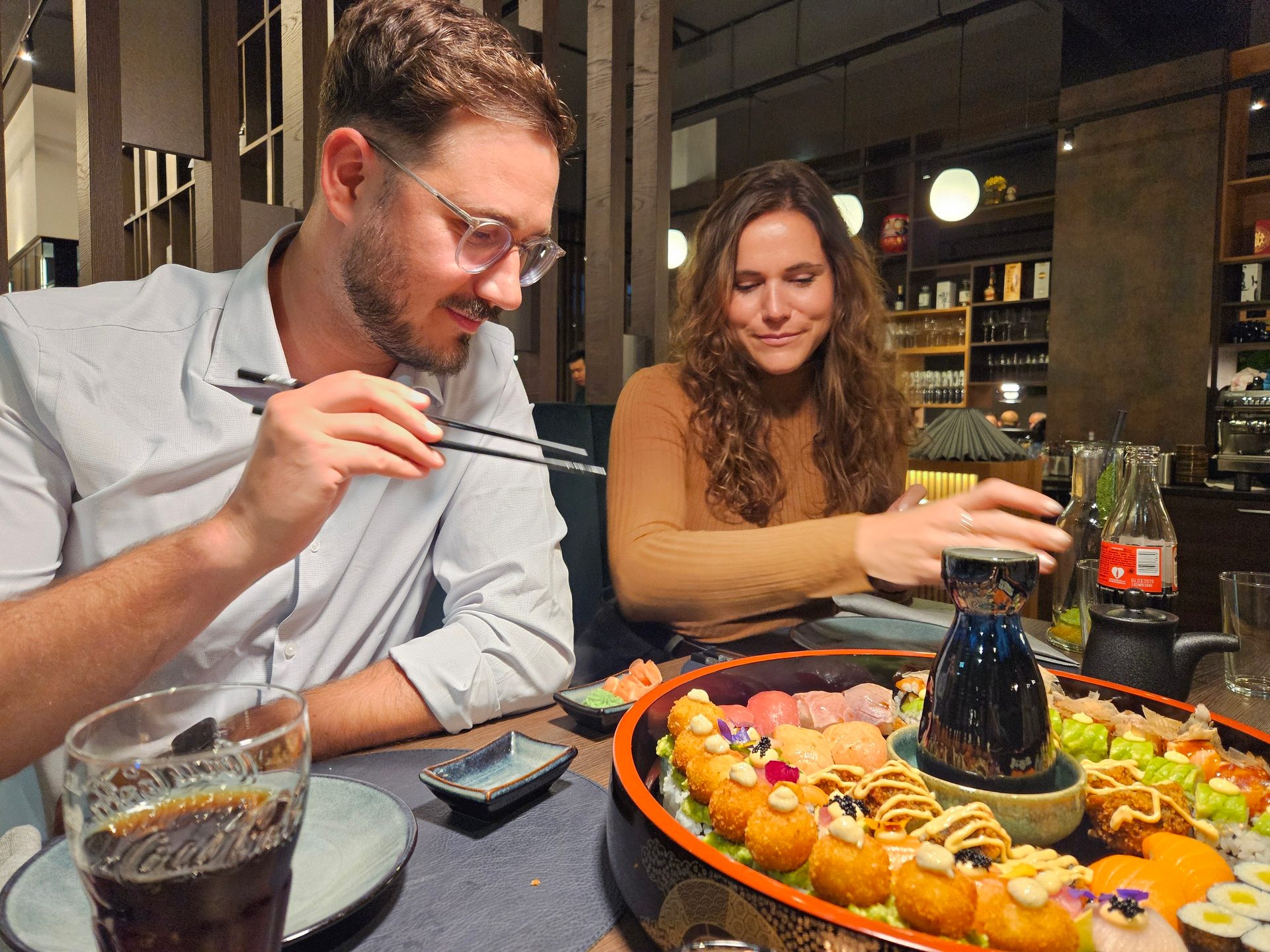 A man and a woman enjoying a large sushi platter at a restaurant, with the man holding chopsticks.