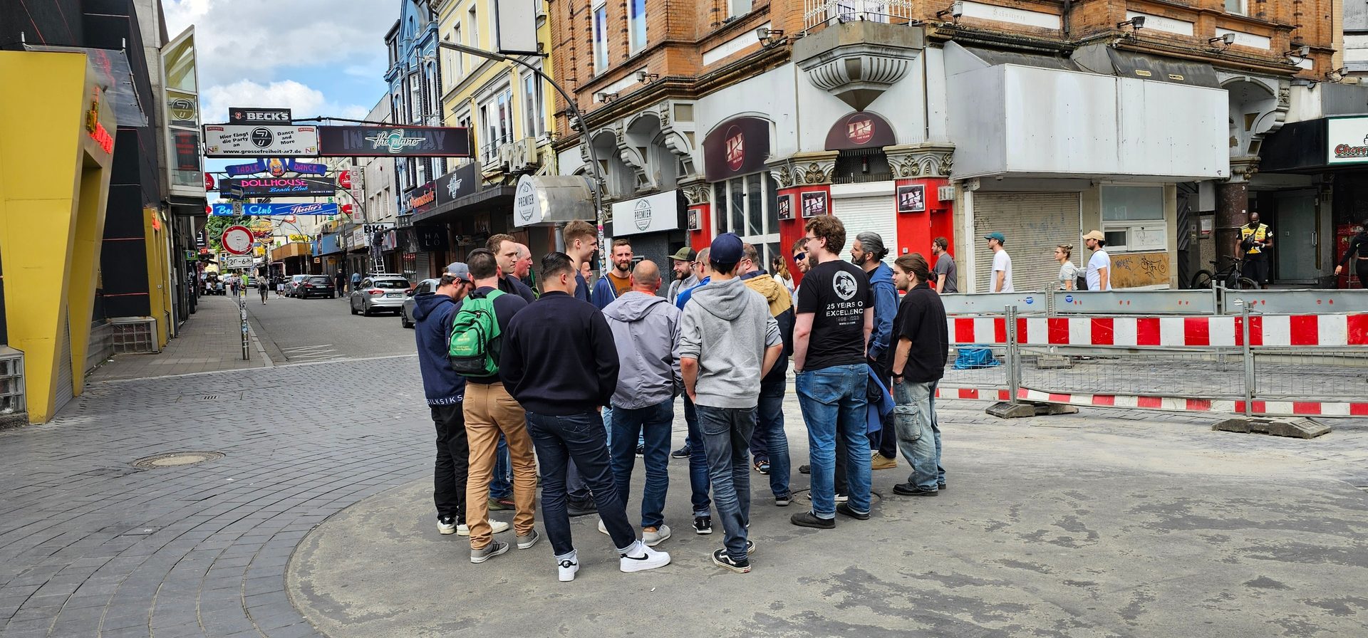 A group of men standing in a circle on a cobbled city street with buildings and shops in the background.