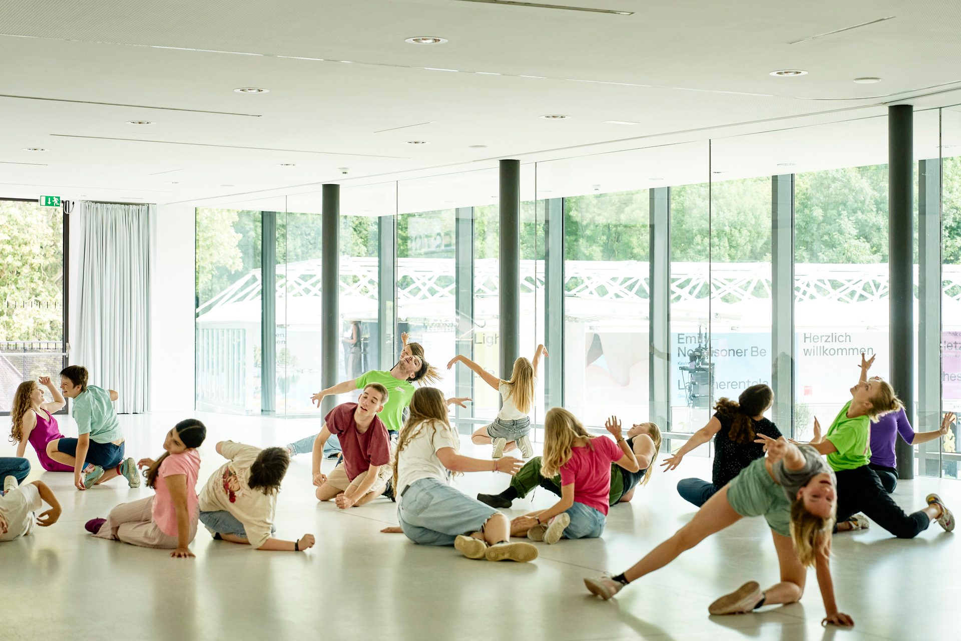 Young people in dynamic poses during a dance or movement class in a brightly lit room.
