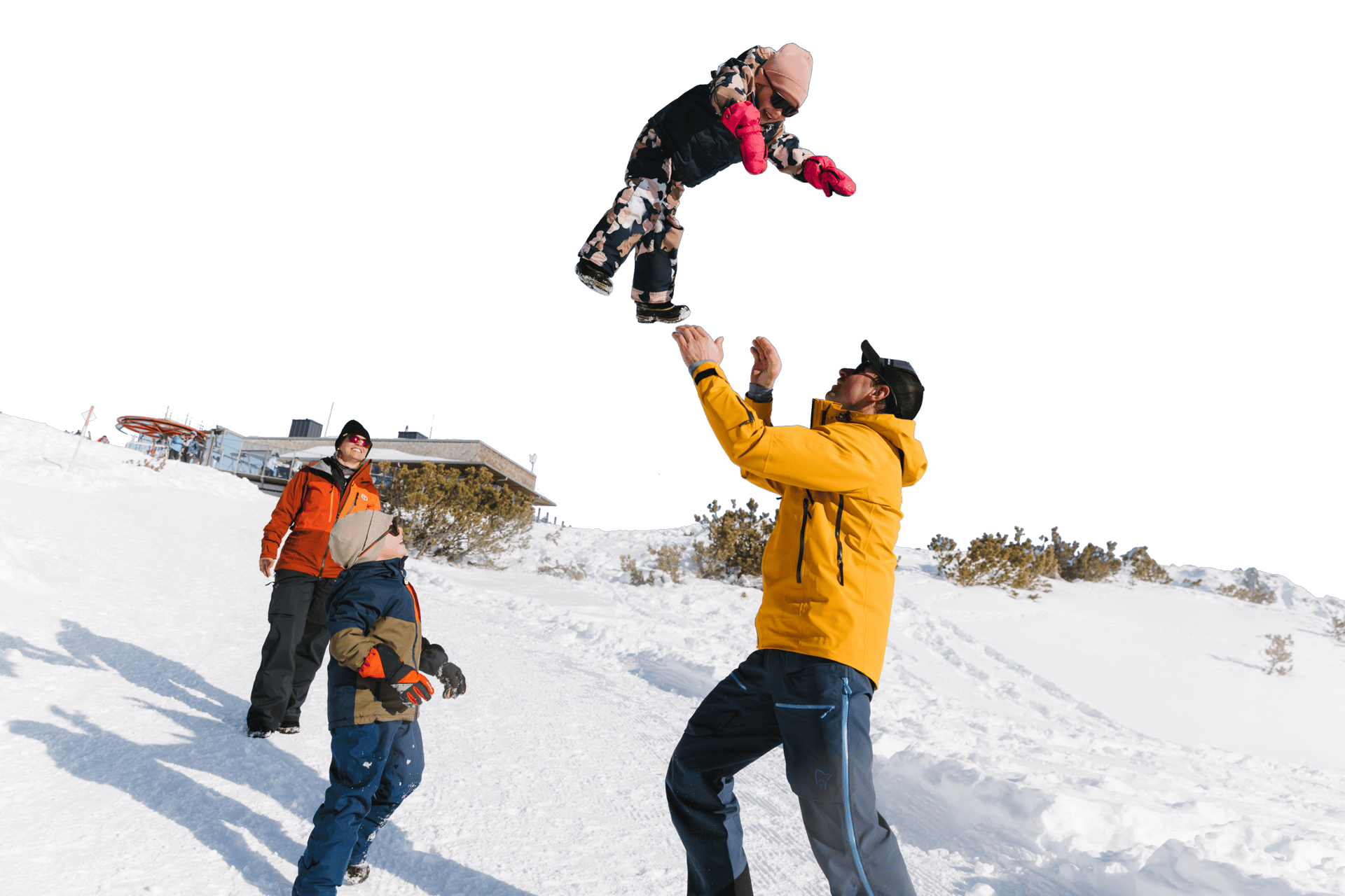 Family playing in snow, adult tosses child high into the air.