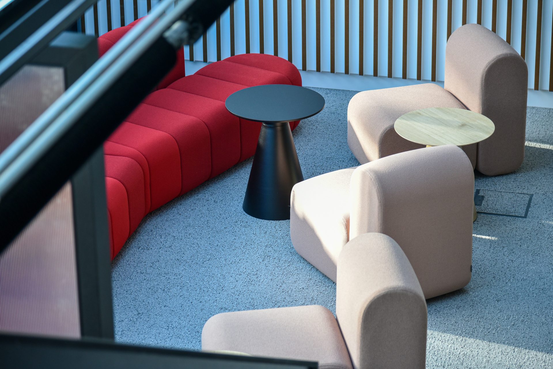 Modern office lounge with red modular sofa, black table, beige modular chairs on a gray carpet.