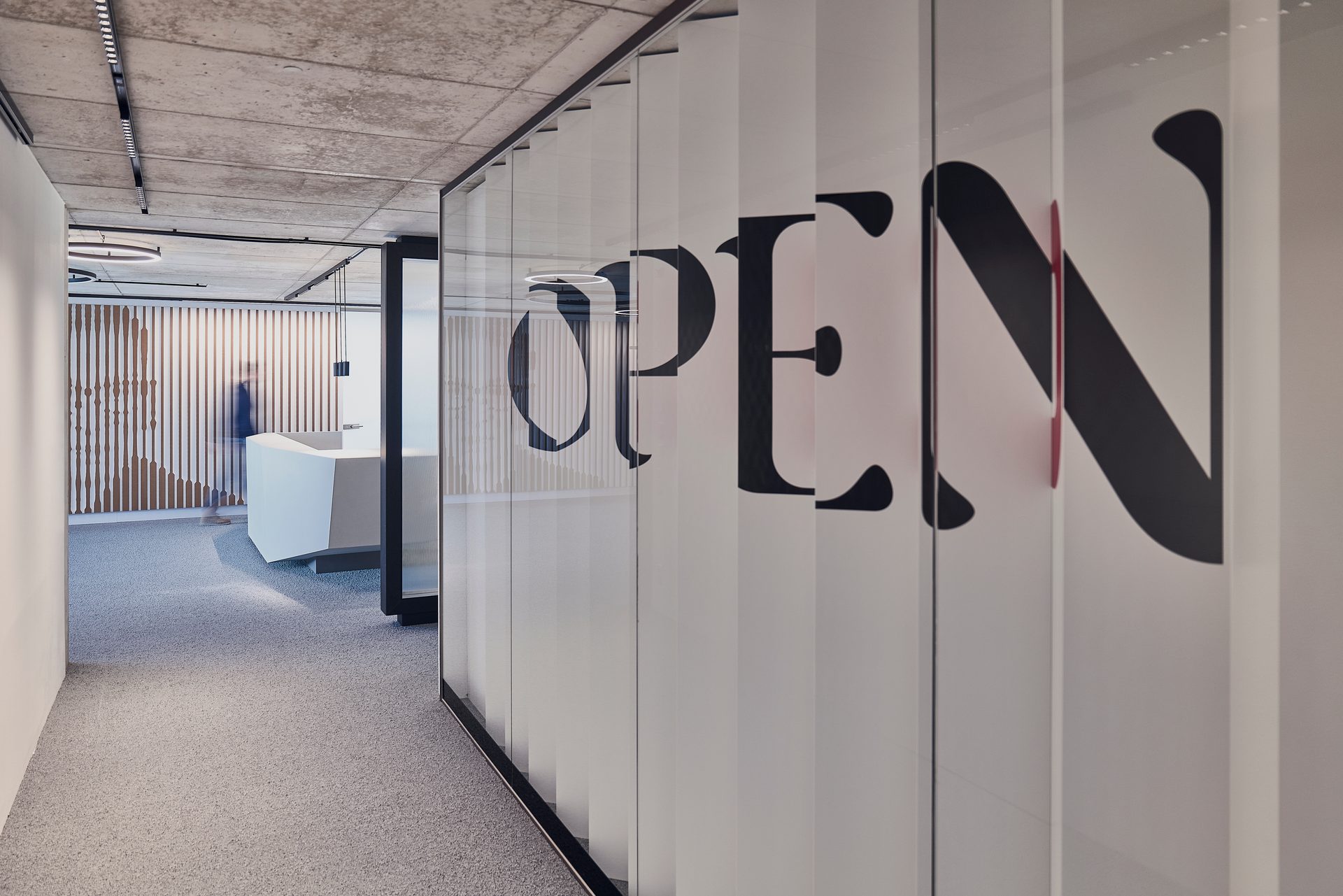 Modern office interior with 'OPEN' sign on glass panels, a white reception desk, and a blurred person.