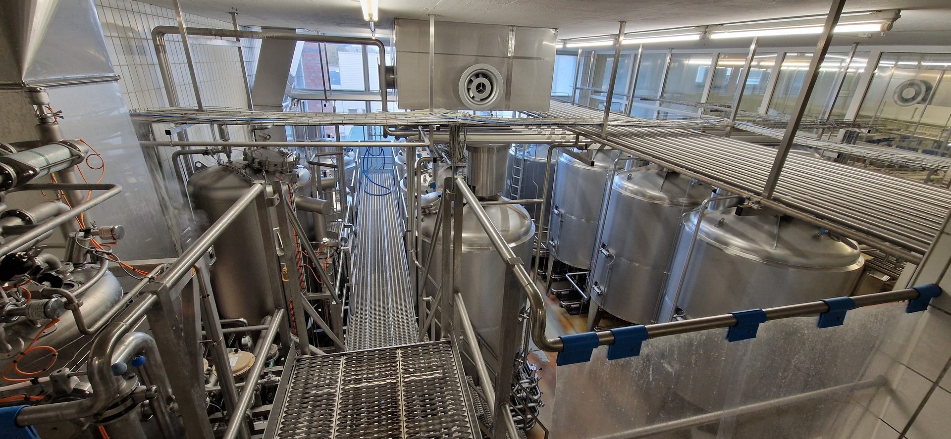 An industrial processing plant featuring multiple large stainless steel tanks, extensive piping, and metal walkways.