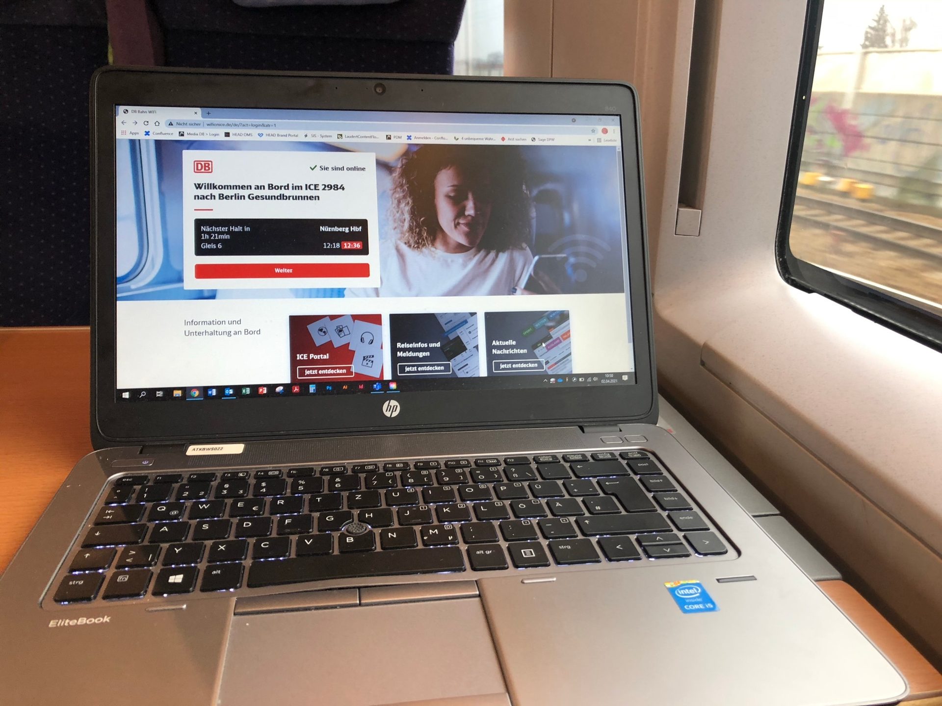 Laptop showing DB train WiFi portal with next stop details, in a moving train carriage.