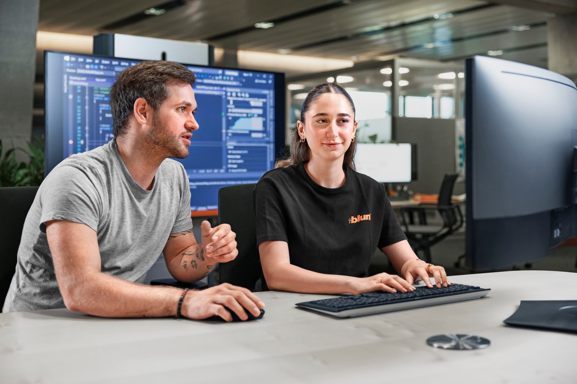 Two coworkers collaborating on computers in an office.