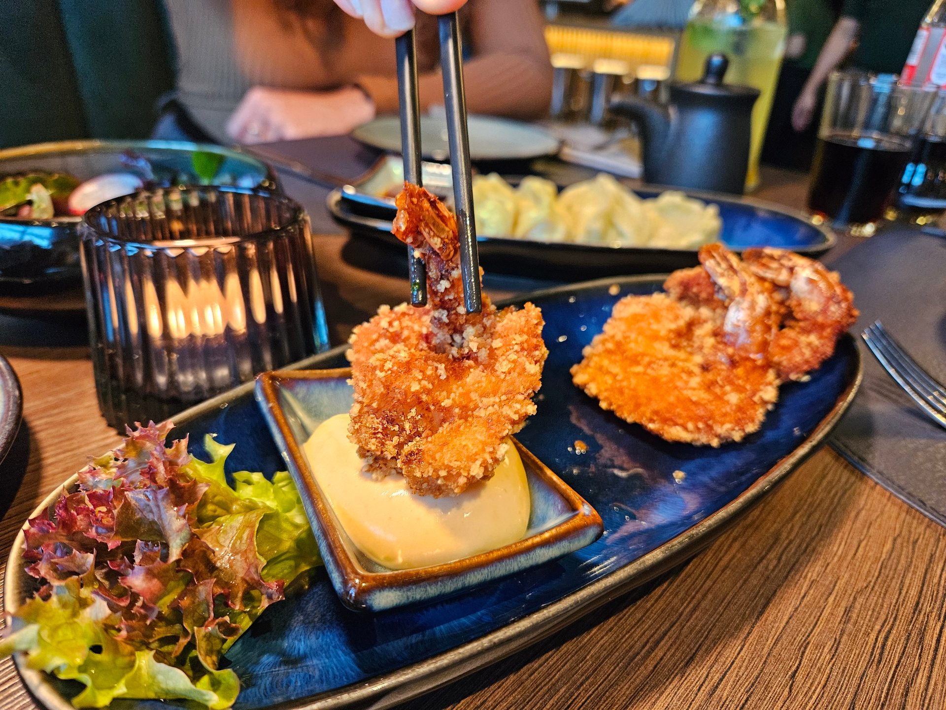 Chopsticks holding crispy fried shrimp over a plate with dipping sauce and lettuce.