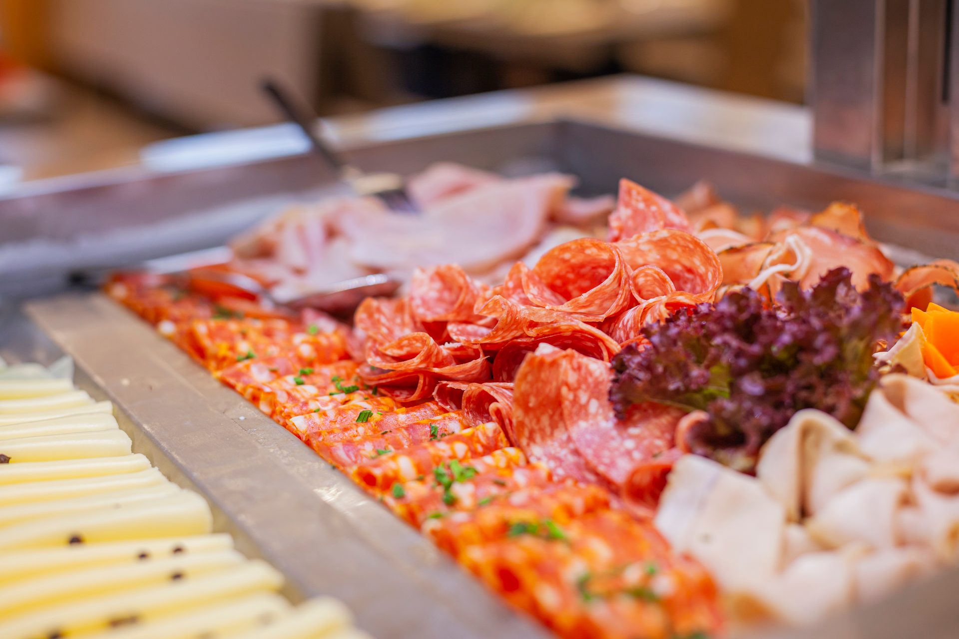 Assortment of cold cuts including salami, pepperoni, and ham, with cheese slices and lettuce on a buffet.