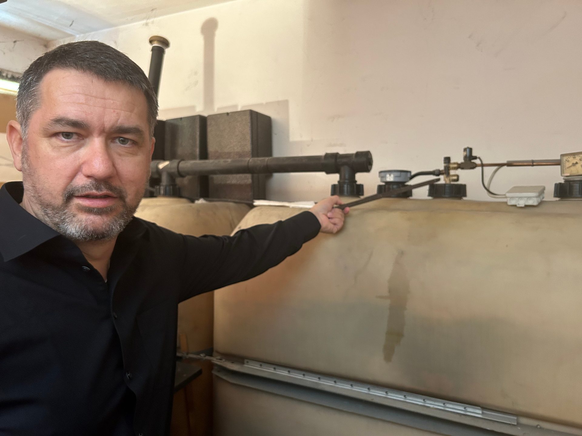 Man pointing at industrial storage tanks with connected pipes and gauges.