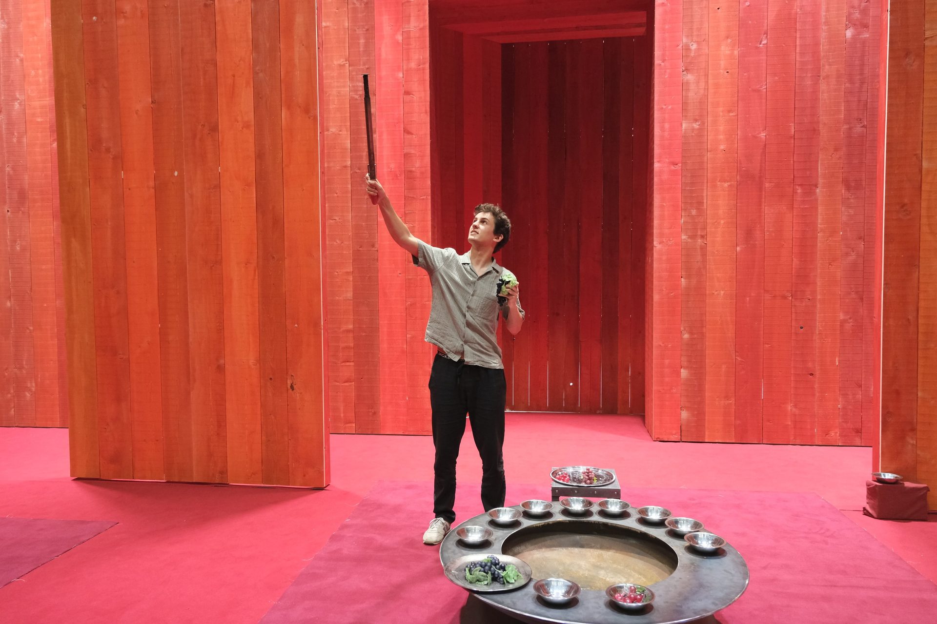 Man in red room holding stick, fruit on table.