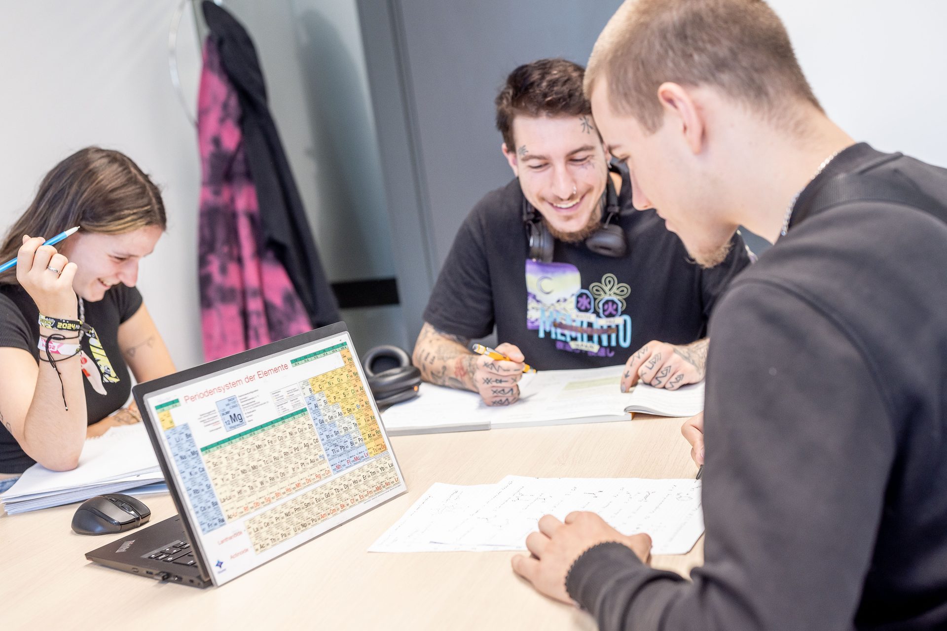 Three students studying, with a laptop displaying the periodic table of elements.