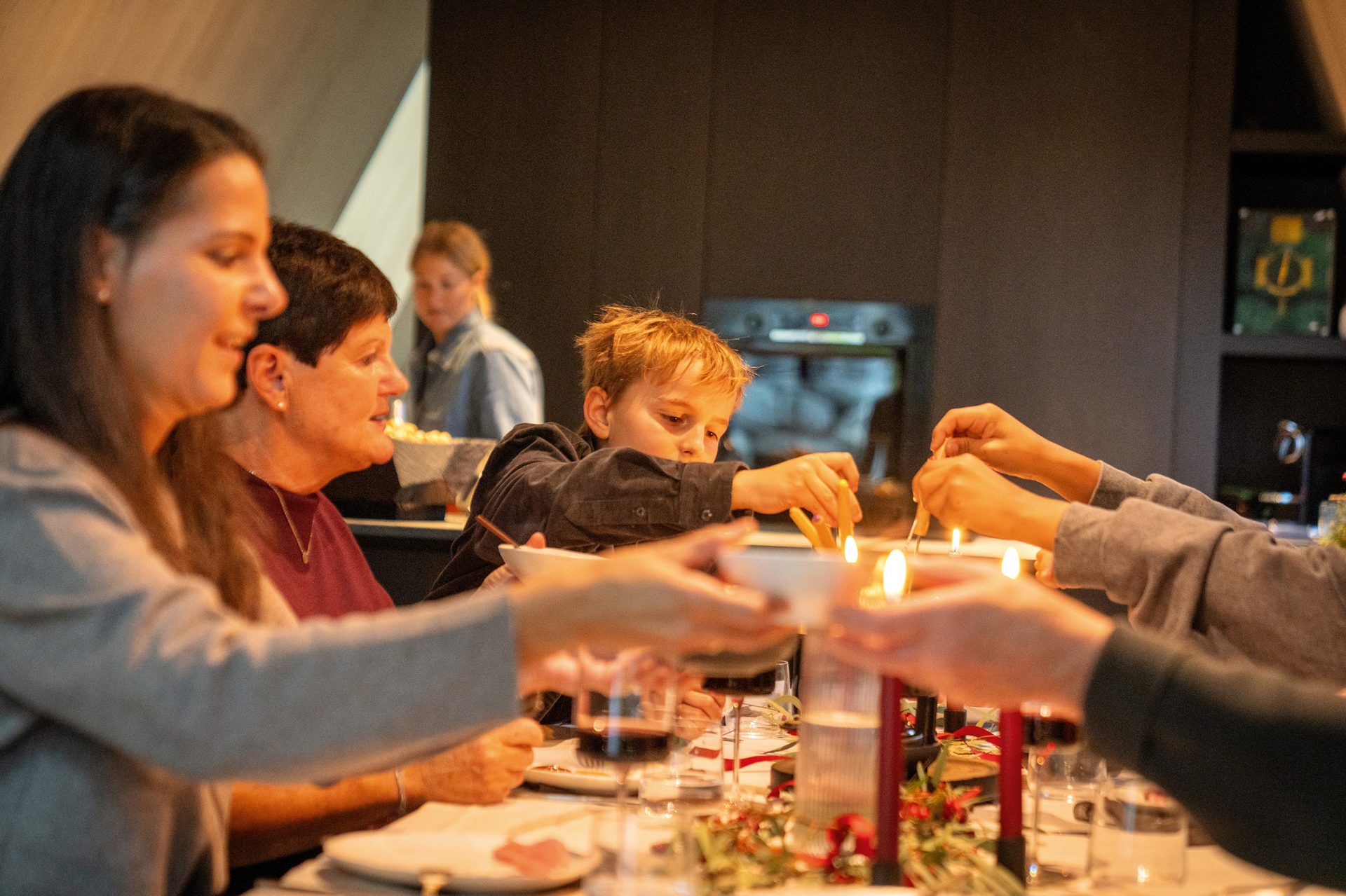 A family, including a child and adults, enjoys a candlelit dinner, reaching for food on the table.