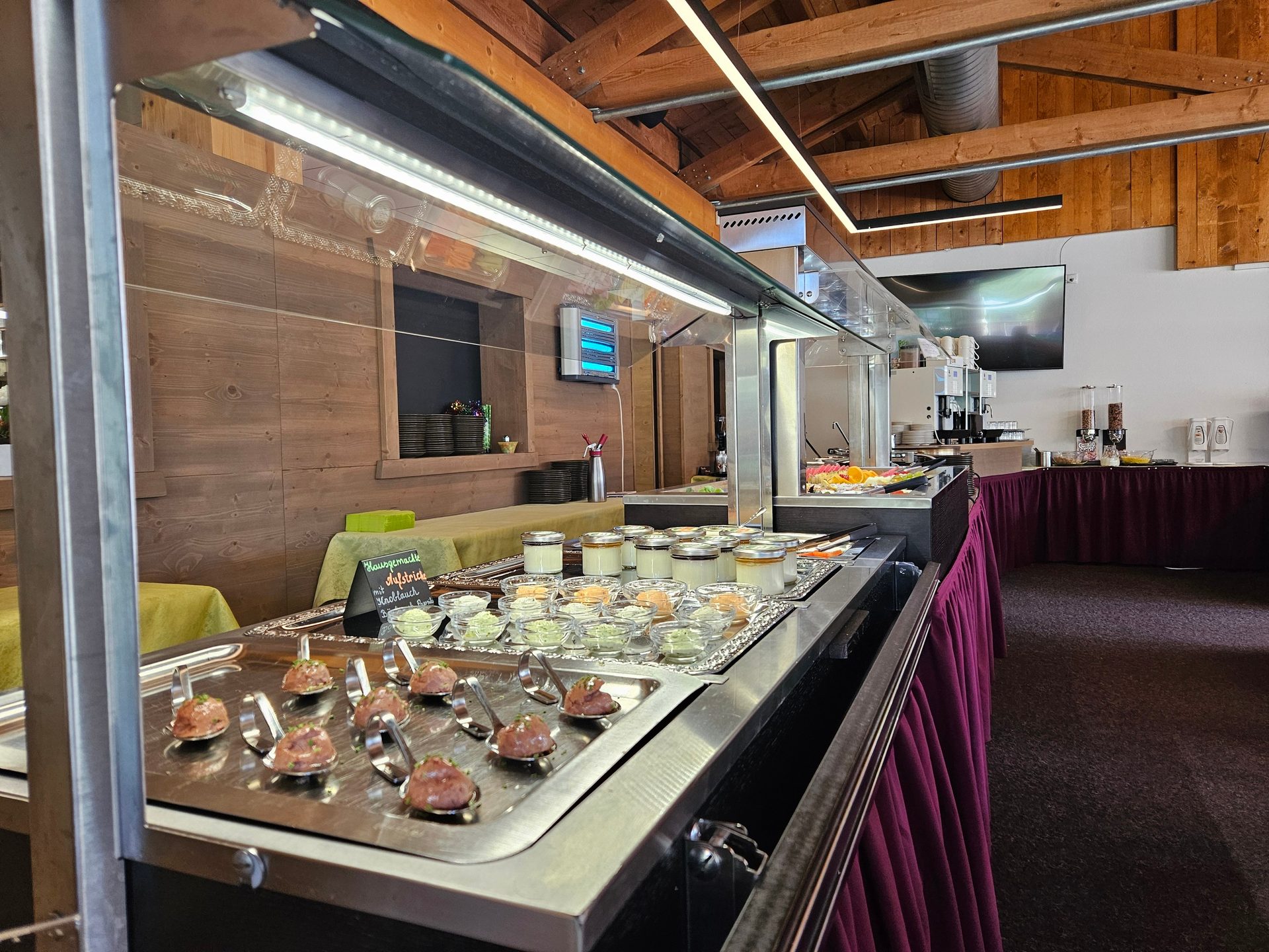 A long, well-lit buffet counter displaying various foods like appetizers and dips in a wooden-paneled room.