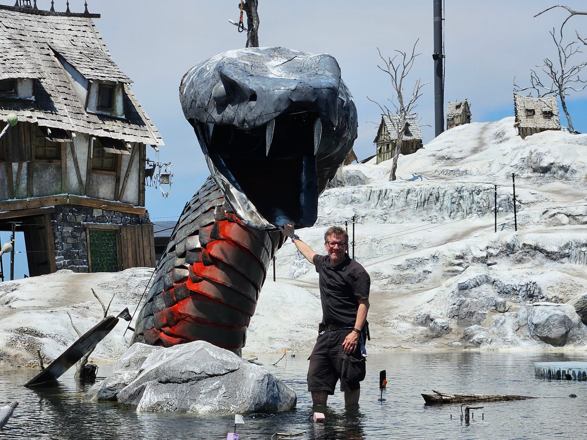 Man in water beside giant snake sculpture in a snowy village set.