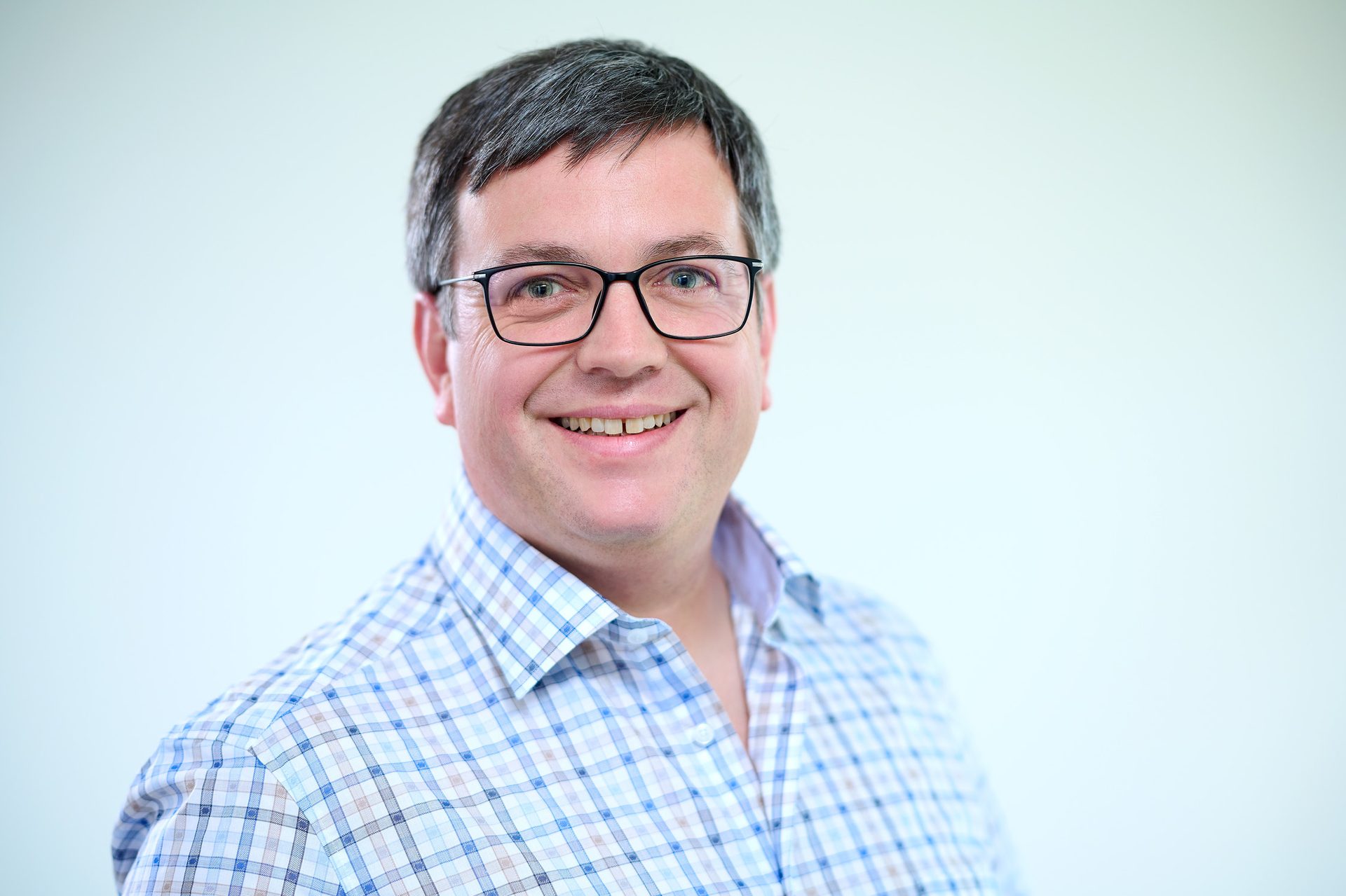 Smiling man with glasses and a plaid shirt.