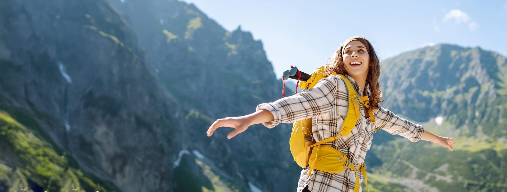 Joyful woman with yellow backpack spreading arms in mountains.