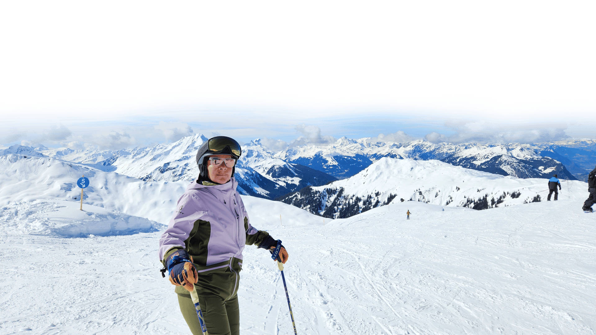 Skier on a snowy mountain slope with majestic snow-covered peaks under a blue sky.