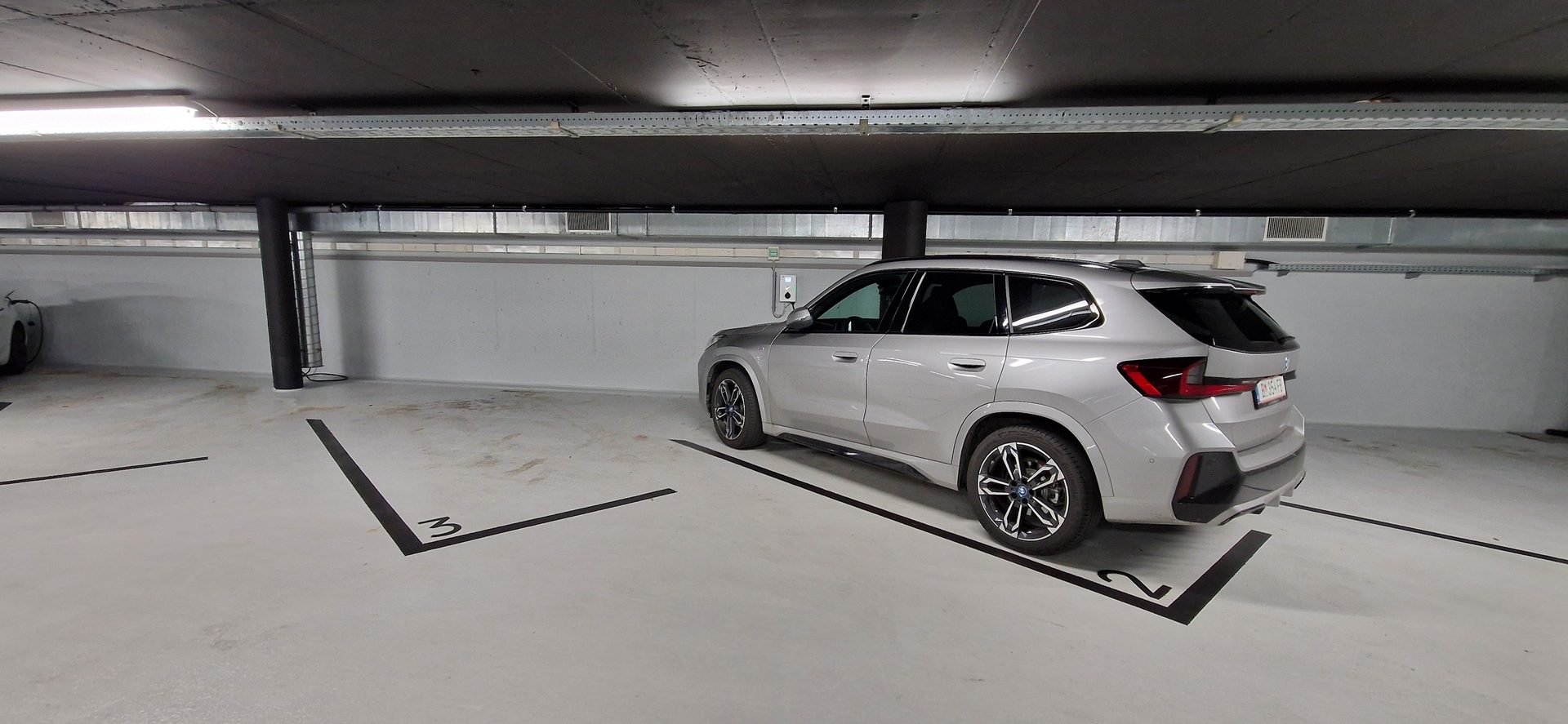Silver SUV in an underground parking garage with an EV charger and marked spots.