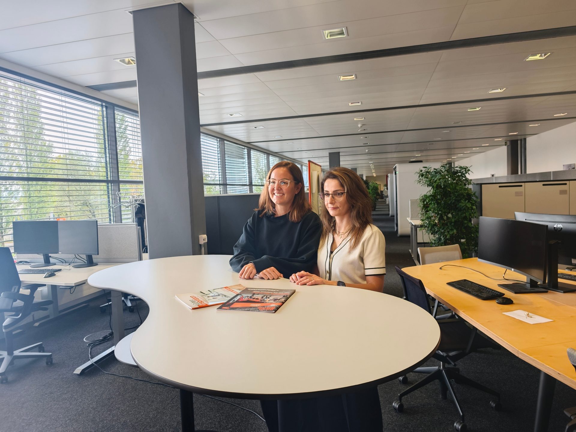 Two women smiling at a white table in a modern office.